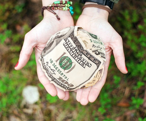 A hand holding out a ball of money, representing charitable giving.