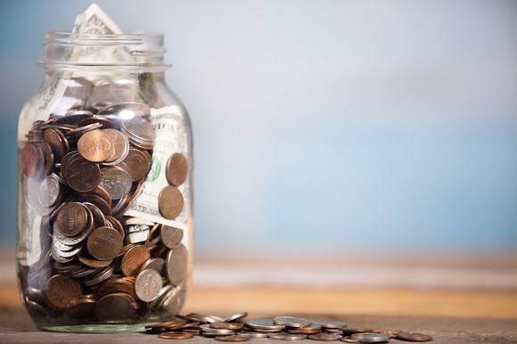 A clear glass jar filled with cash and coins.