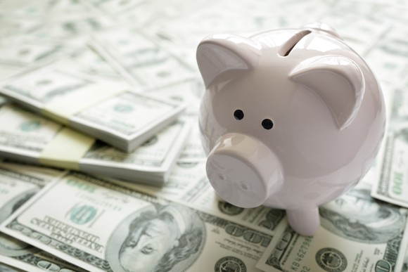 A white piggy bank sits on top of a pile of money.