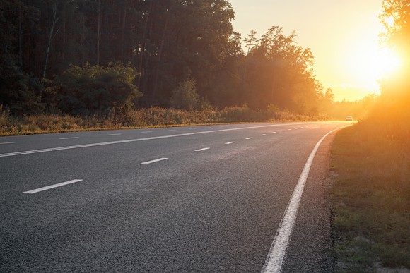 An empty road leads to a setting sun.