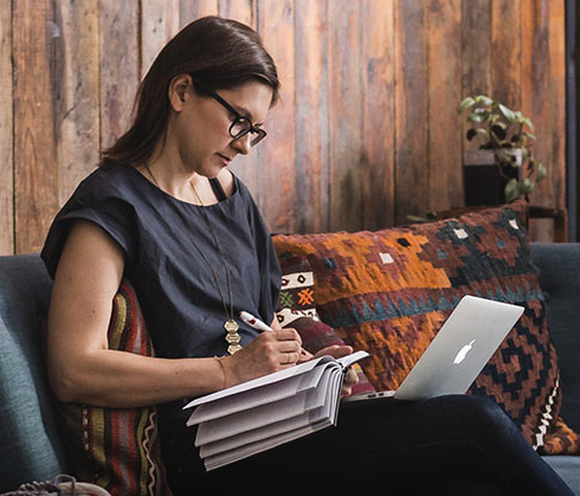 Casually dressed businesswoman on couch taking notes while looking at her laptop.