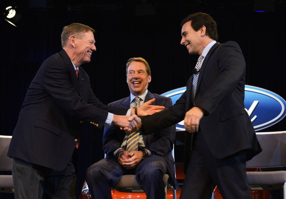 Alan Mulally shaking hands with Mark Fields during a press conference.