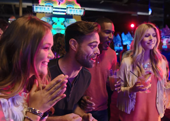 Four adults playing a video game at Dave & Buster's.