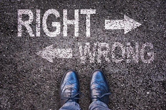 A pair of black dress shoes viewed from above, standing on pavement on which is written "right" and "wrong," with arrows going in two directions