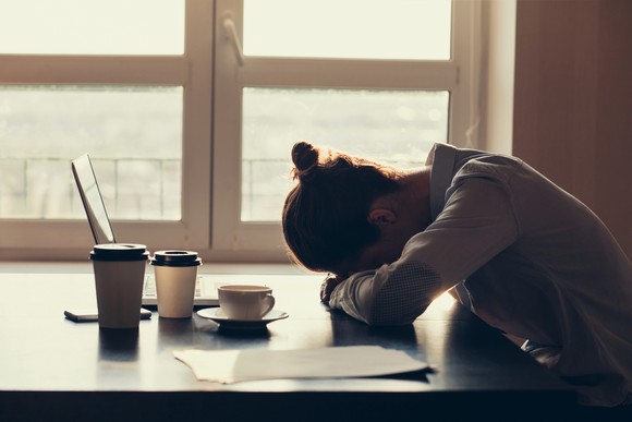 Woman in shadow with head on desk, seeming upset or sad