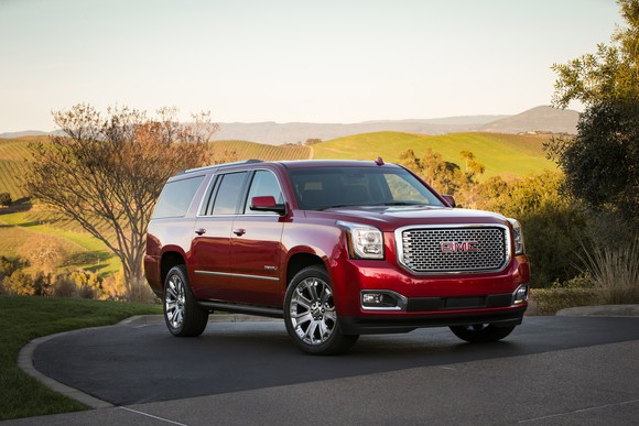 A red 2017 GMC Yukon Denali XL SUV in a sunlit country setting.