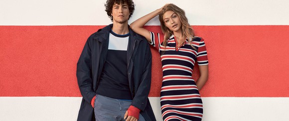A man and woman in Tommy Hilfigir clothing stand in front of a red wall.