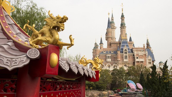 A dragon carving smiles in the foreground in front a castle at Disney Shanghai