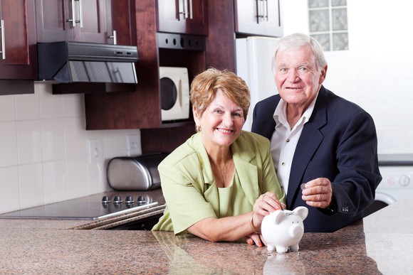 An older couple in a kitchen with a piggy bank.