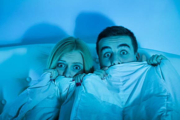 Frightened couple in bed, drawing covers over their mouths