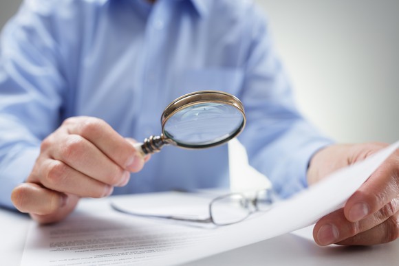A man looks at a financial document with a magnifying glass.