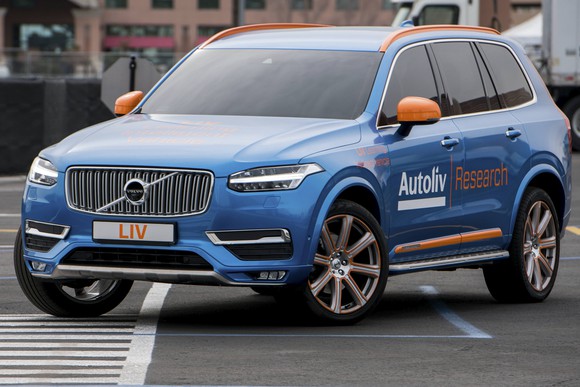 A blue Volvo SUV with Autoliv emblems on a city road.