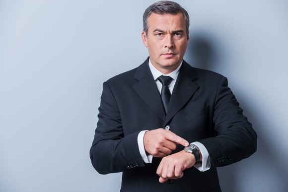 A businessman pointing at his watch, implying that the tax deadline is approaching.