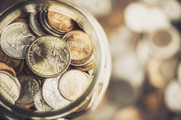 Coin jar resting on top of a pile of coins.