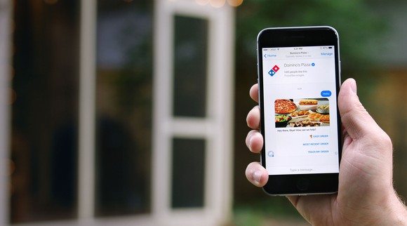Hand holding a smartphone displaying ordering from Domino's via Facebook Messenger