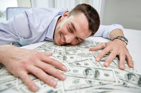 A smiling man laying his head on a pile of cash.