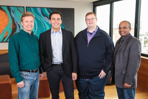 The four men are standing in a conference room.