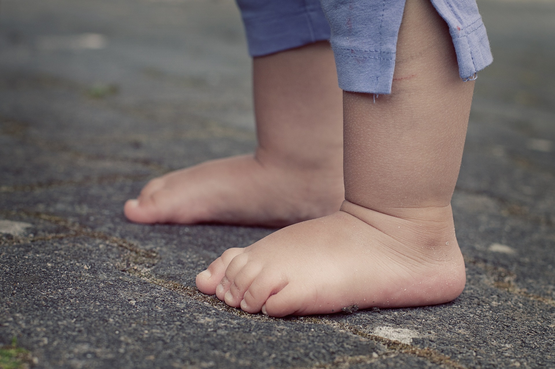 A toddler's legs, from the knees down, on pavement