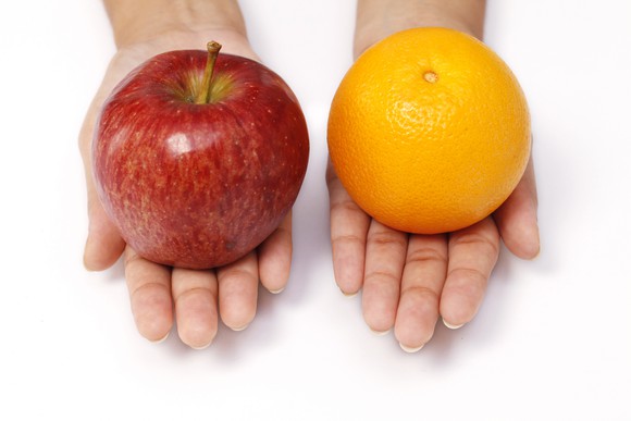 Someone holding out an apple in one hand and an orange in the other.