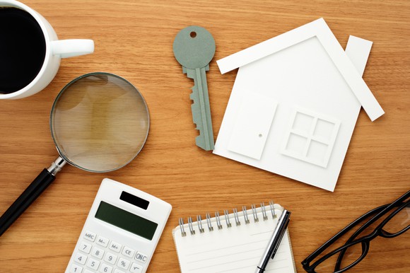 Calculator, paper house, and magnifying glass on a table