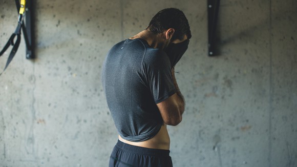 A man wipes sweat off his face with his Lululemon shirt during a workout.