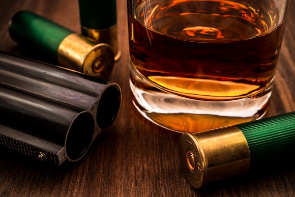 A glass of whiskey and a double-barreled shotgun with ammo