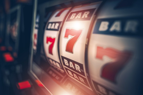 A slot machine slows to nearly land on three 7's in a row.