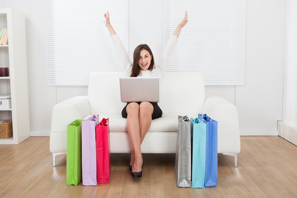 Woman with laptop on her lap and shopping bags at her feet.