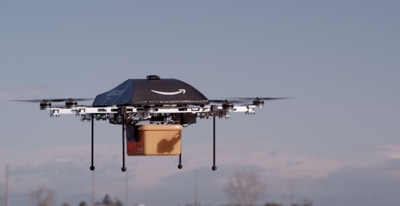 An Amazon-branded drone mid-flight holding a package in a yellow container.