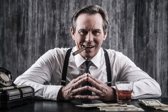 A wealthy businessman sitting at a table with hands crossed.