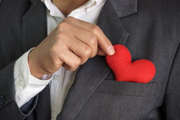 A businessman putting a red heart into his suit pocket.