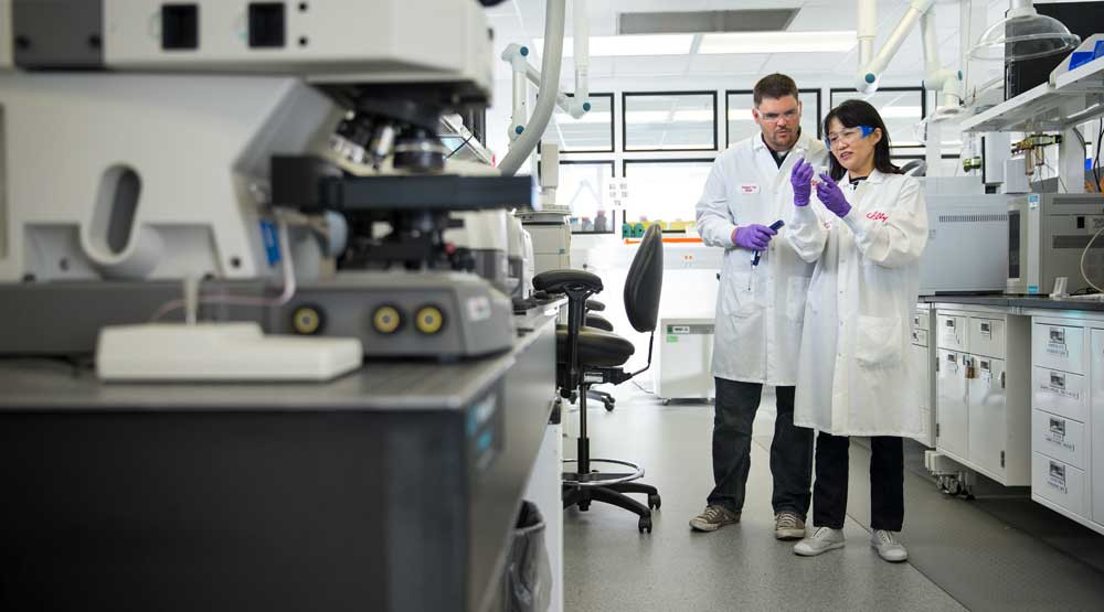 A man and woman in lab coats examine a vial of liquid.