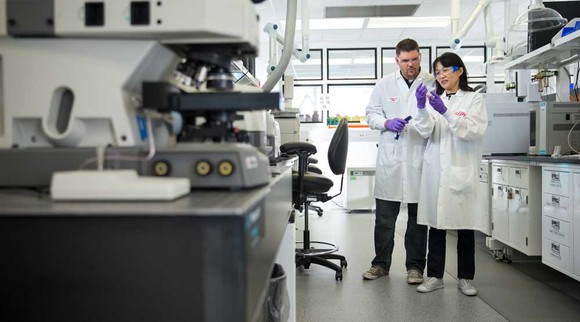 A man and woman in lab coats examine a vial of liquid.
