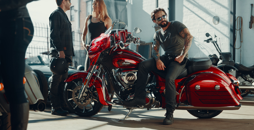 A male model wearing sunglasses sits on the new Indian Chieftain Elite in candy-apple red on a busy showroom floor