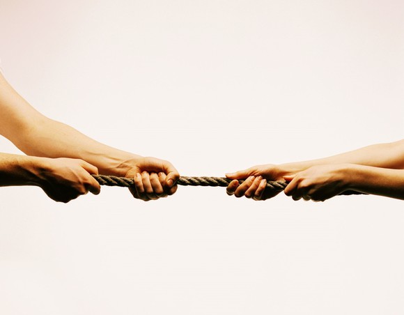 Two pairs of hands tugging on opposite ends of a rope
