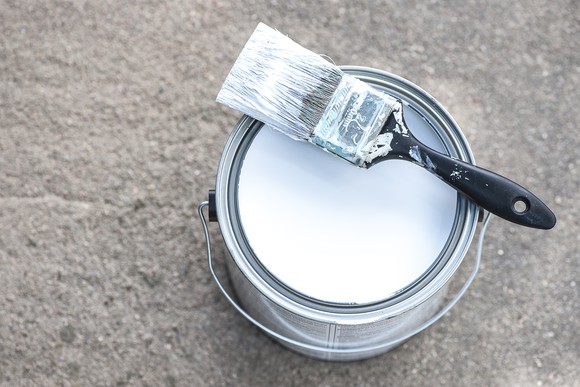 Can of white paint with paintbrush.