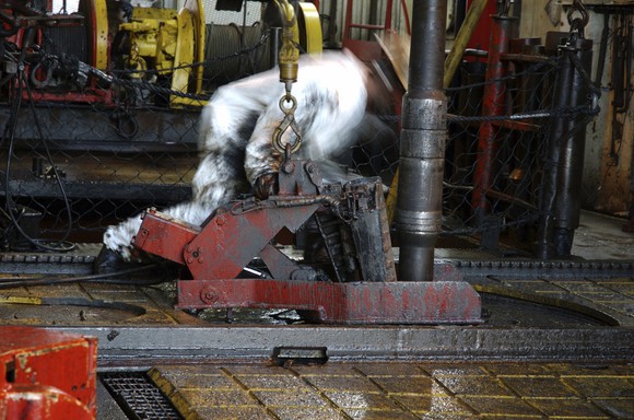 An offshore oil worker connecting a drilling pipe on a rig platform