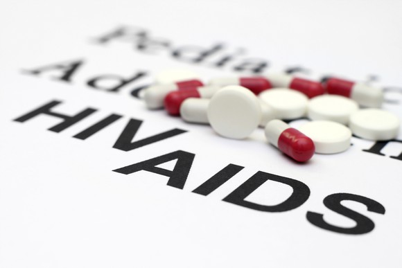 Pills and capsules on a surface that reads "HIV" and "AIDS."