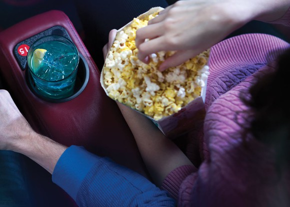 Hand in popcorn and drink in cup-holder in movie theater seat