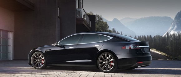 Black Tesla model S parked in front of house with mountains in background.
