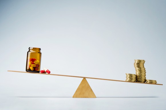 Money outweighing bottle of pills on scale