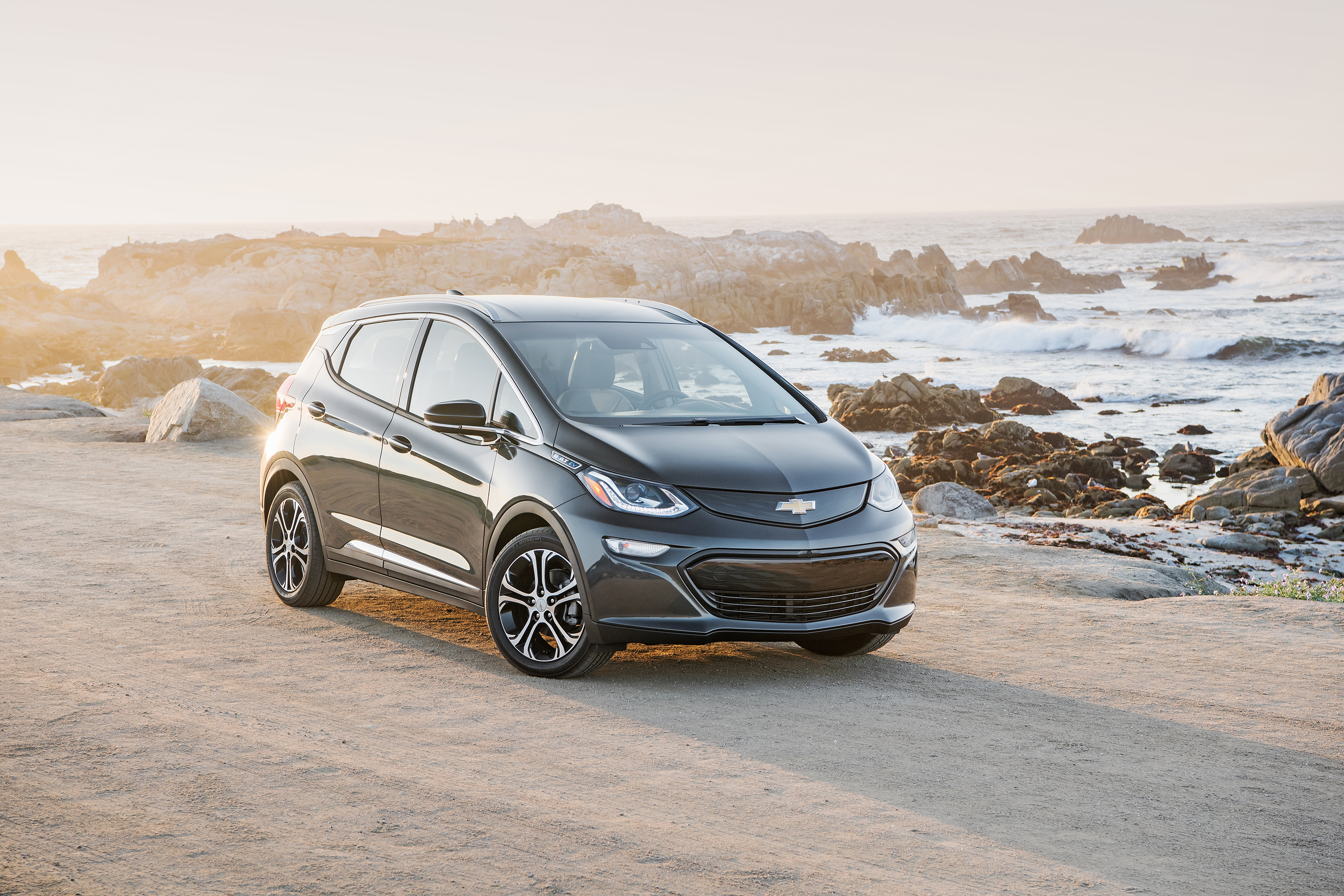 A black Chevrolet Bolt EV before a rocky waterfront.