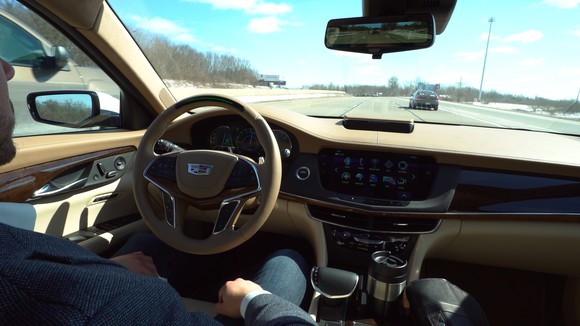 A view of the dashboard of a Cadillac on the highway: The driver's hands are off of the steering wheel.
