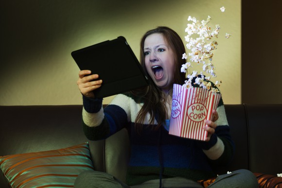 Woman watching a tablet screen spills popcorn in excitement.