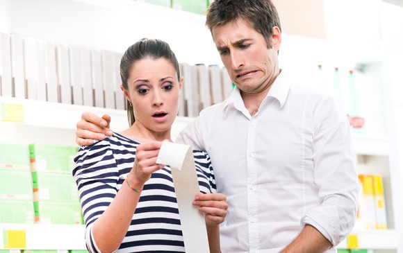 A young couple horrified by the prices on their receipt, implying high inflation levels.