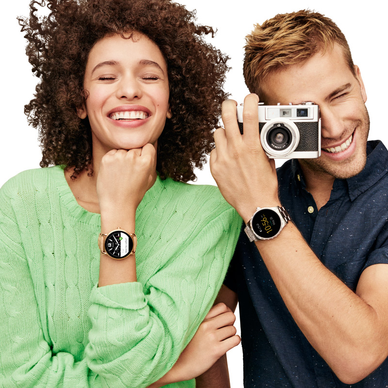 A man and a woman posing with a camera and wearing Fossil watches.