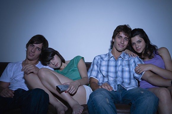 Friends watching TV in darkened room.