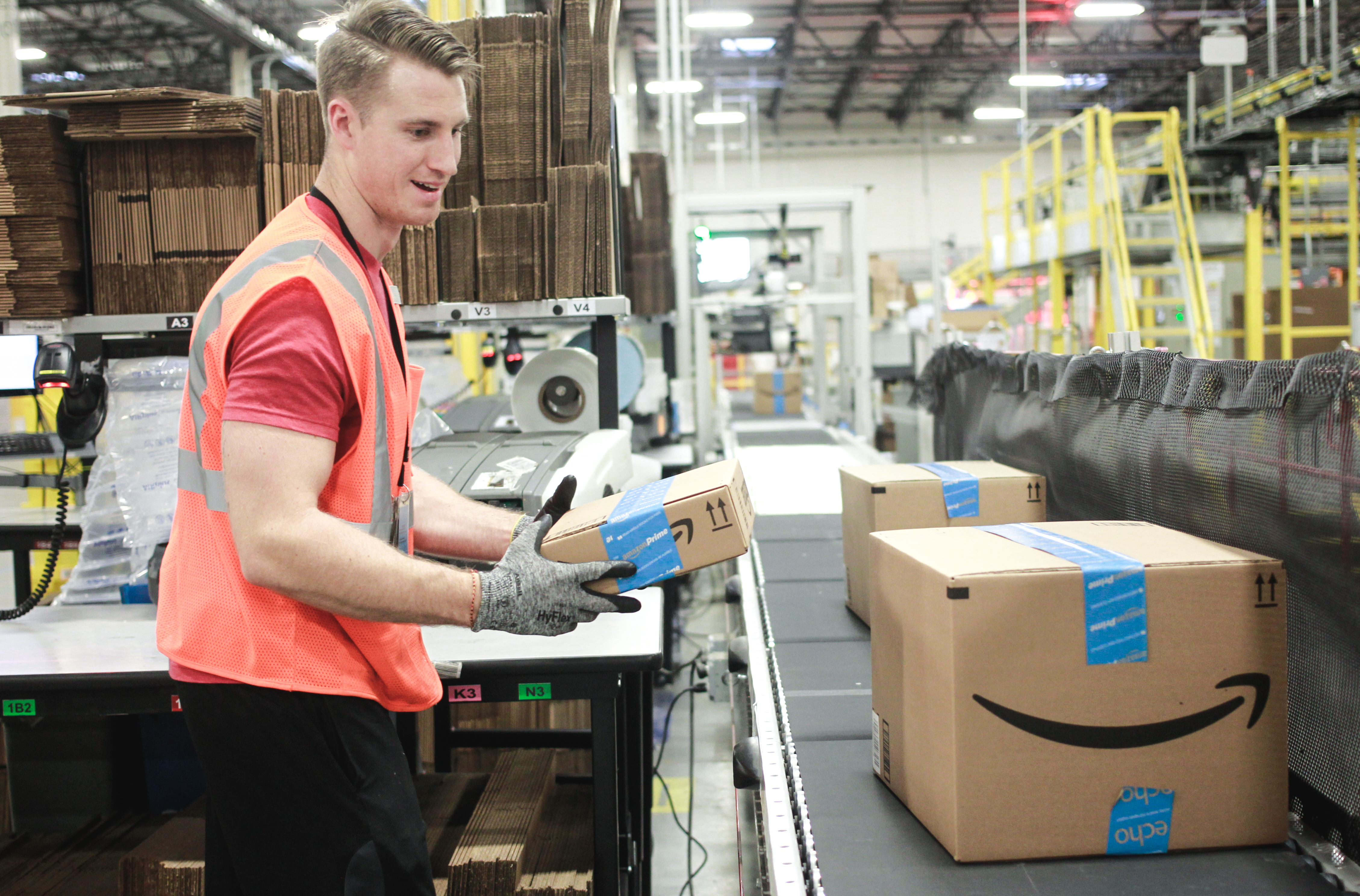 A worker placing Amazon packages on a conveyor belt.