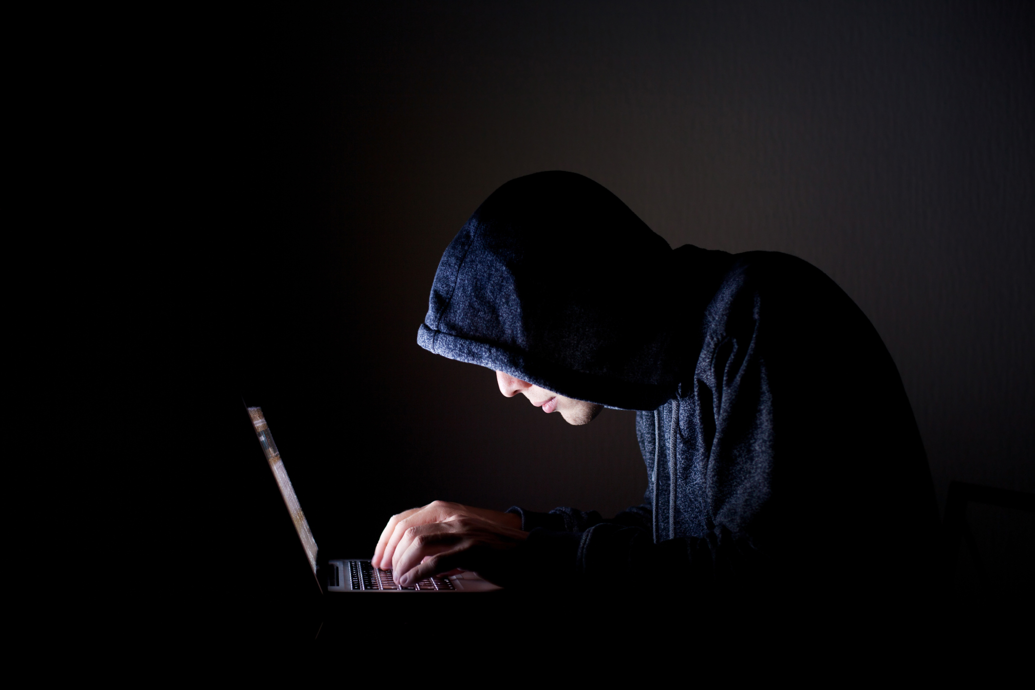 Man in dark hoodie leaning over laptop computer