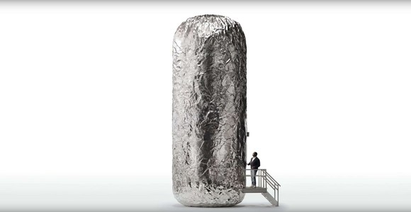 A giant burrito stands erect while a person climbs a set of stairs leading into it as if it were a building.